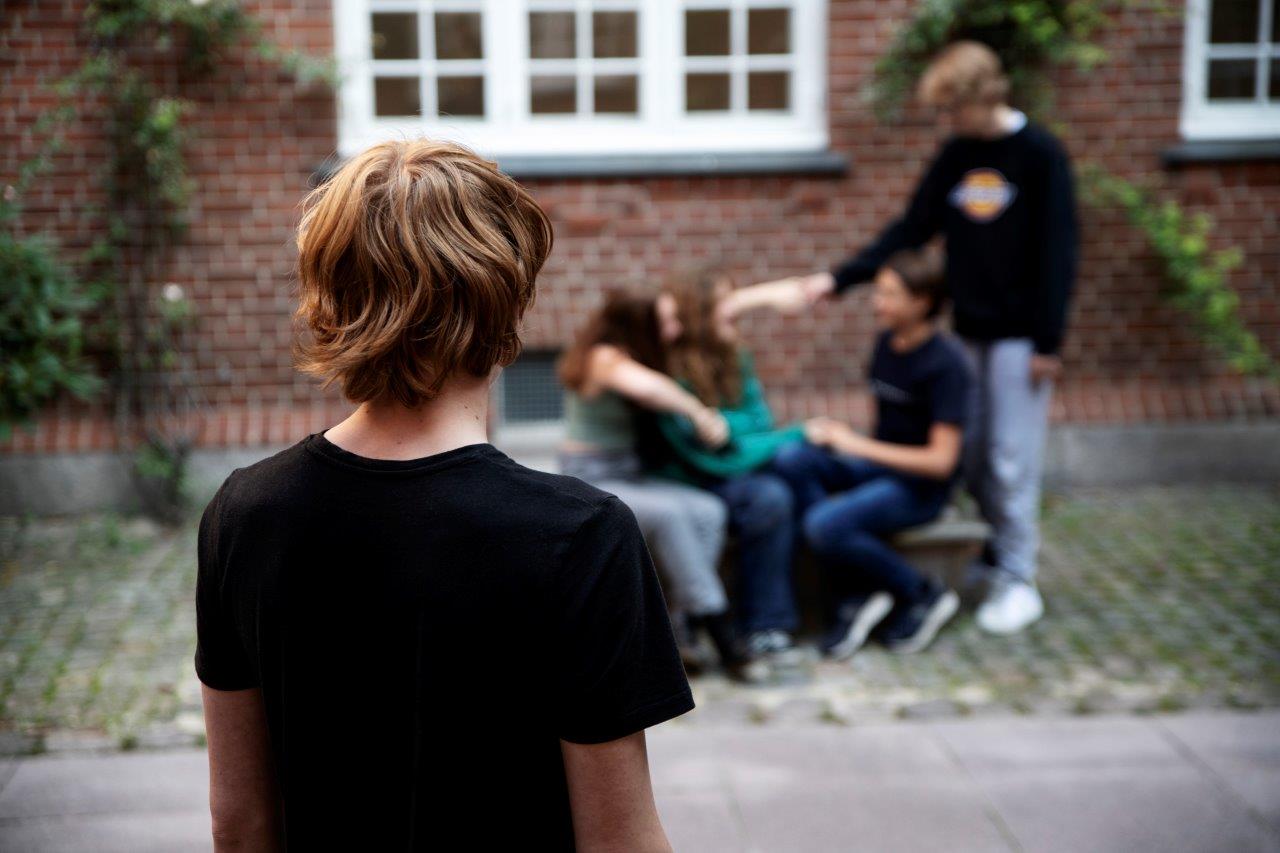 Ensom dreng En ensom dreng står alene, og kigger på en gruppe unge der hygger sig.